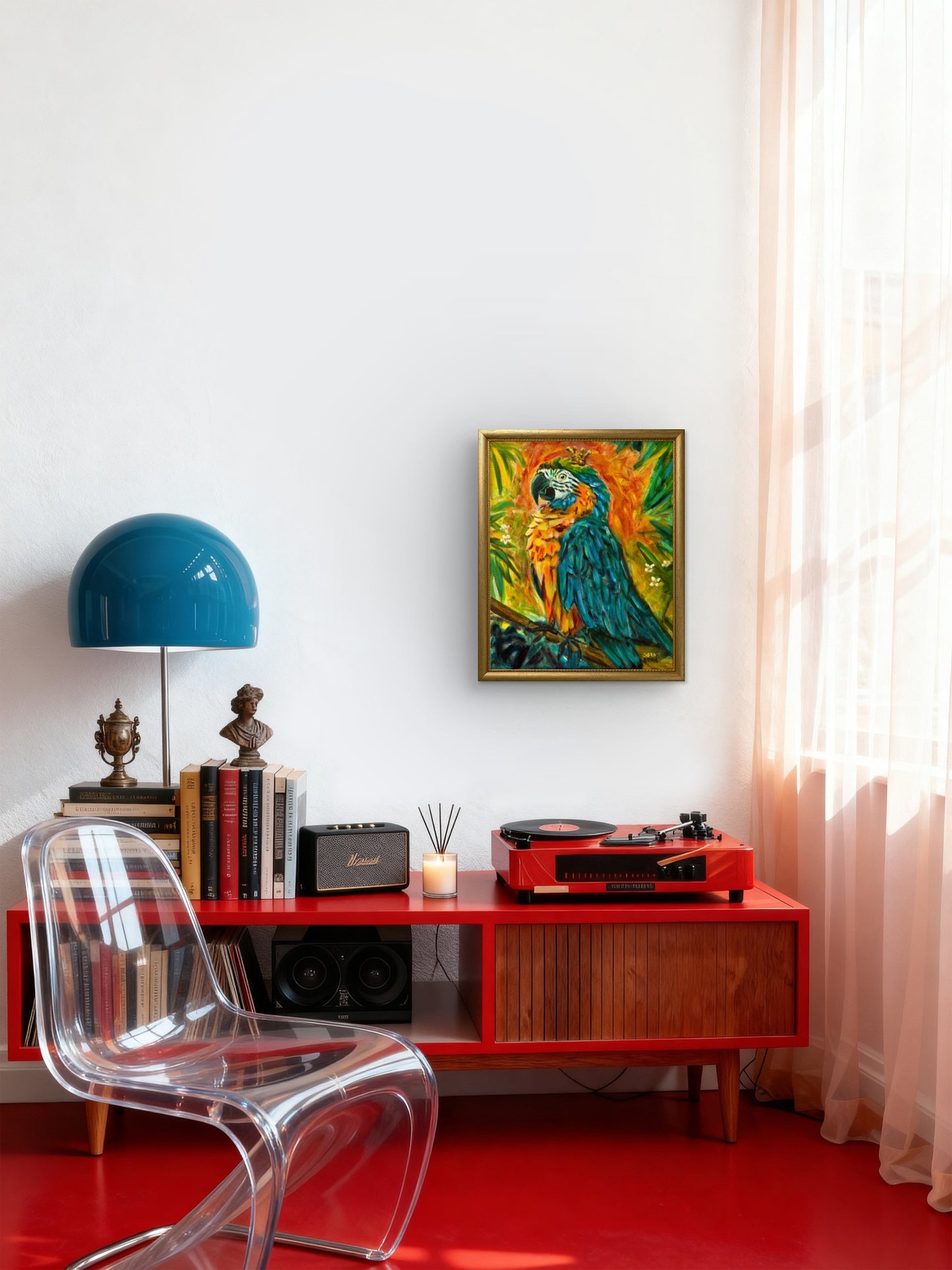 A colorful framed art print of a parrot hanging on a white wall above a red media console in a modern room setting with a clear chair, blue lamp, and red floor.