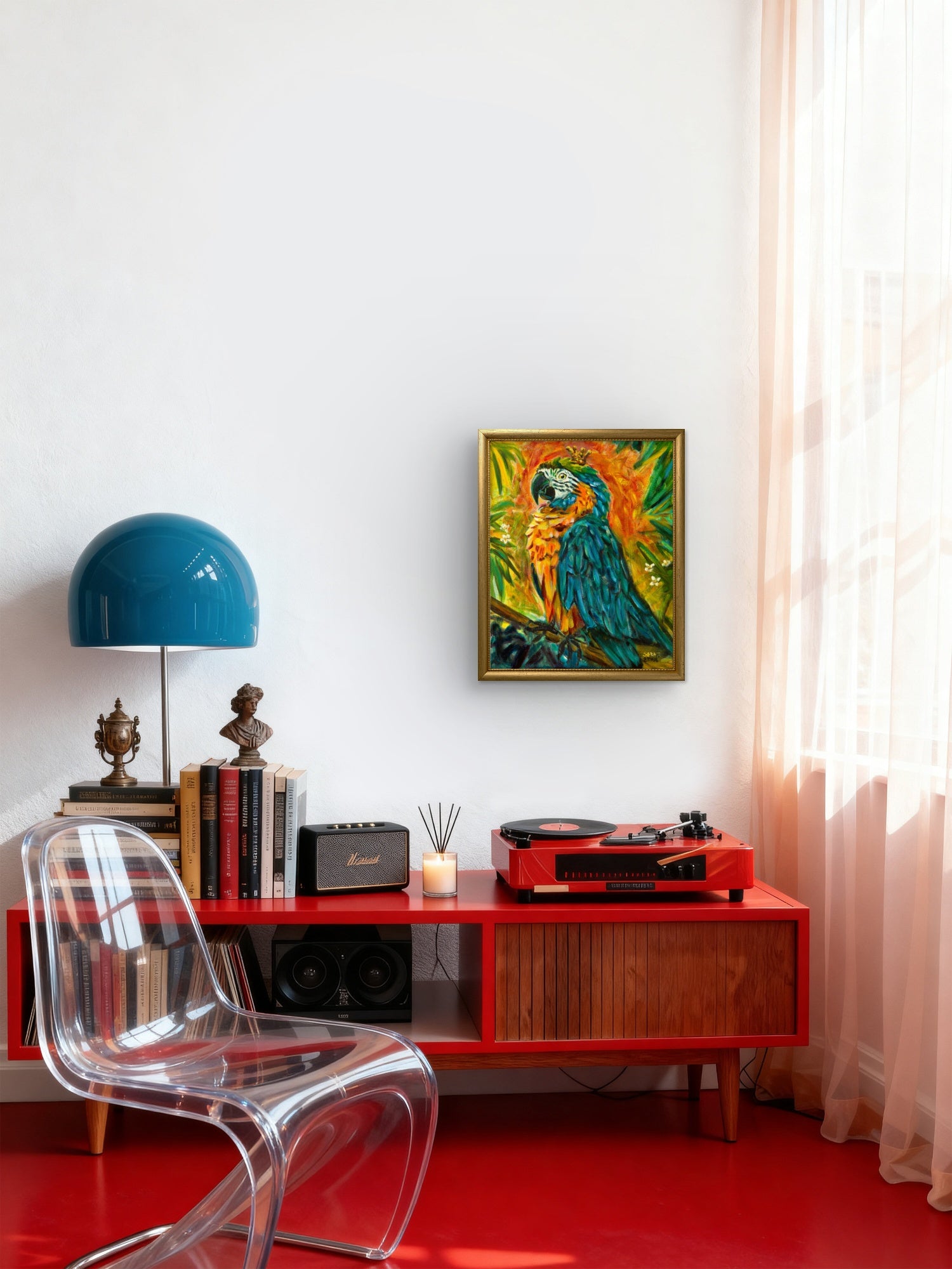 A colorful framed art print of a parrot hanging on a white wall above a red media console in a modern room setting with a clear chair, blue lamp, and red floor.