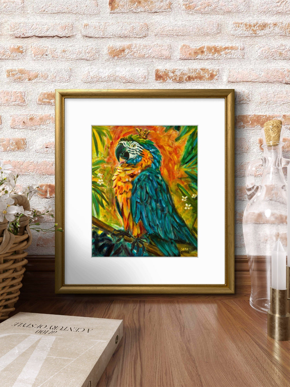 A framed colorful painting of a blue-and-yellow parrot hanging on a brick wall above a wooden surface, with a book and glass bottle nearby.